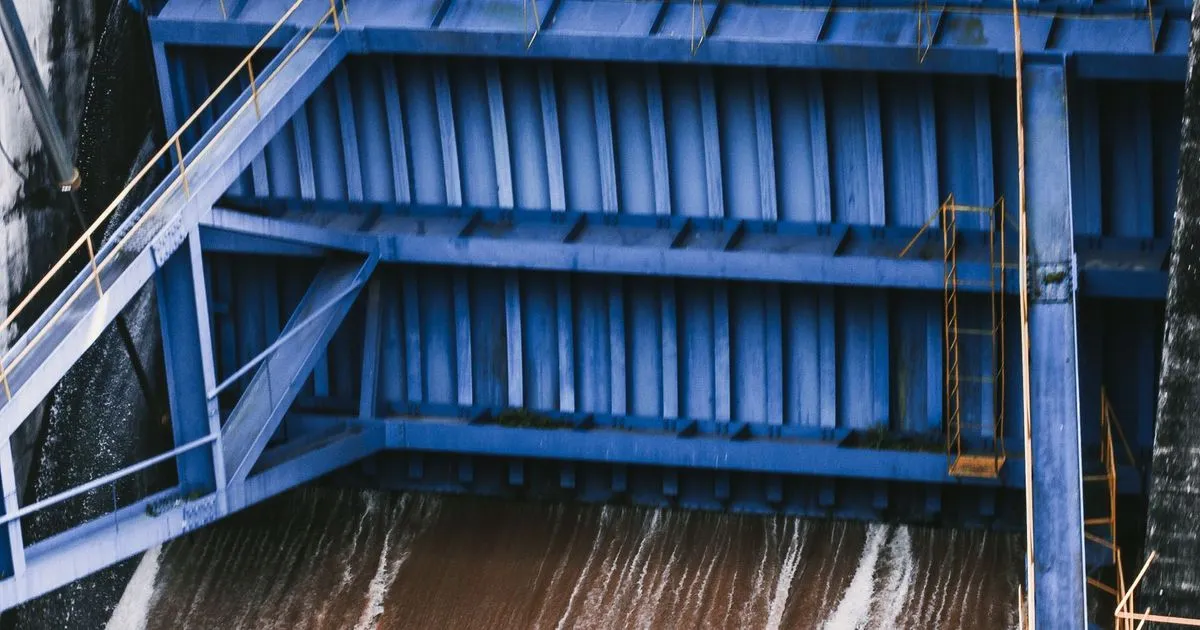 Blue steel dam gate panel above flowing water at a dam, an example of hydraulic steel gate fabrication