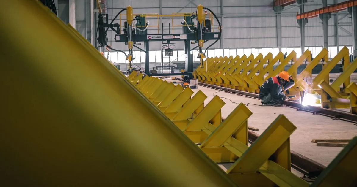 Rows of yellow fabricated steel structural sections laid out on a shop floor, ready for a trial assembly of a steel structure