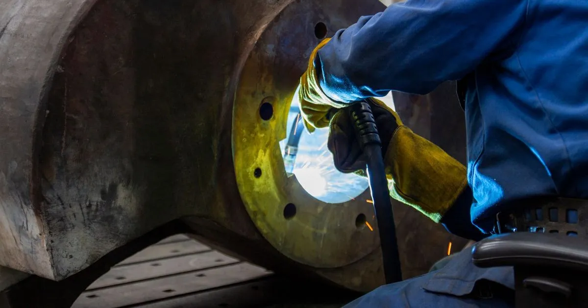 Welder in gloves welding a heavy steel component with thick walls, the kind of joint where Z35 through thickness steel is considered